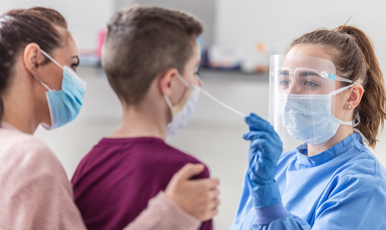 Sanitaria con mascarilla y pantalla protectora haciendo un test COVID a un niño