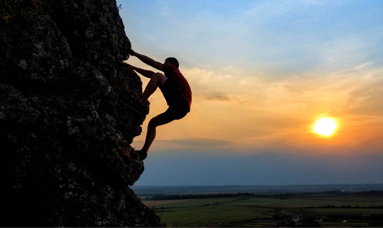 Hombre escalando una pared rocosa con el atardecer de fondo