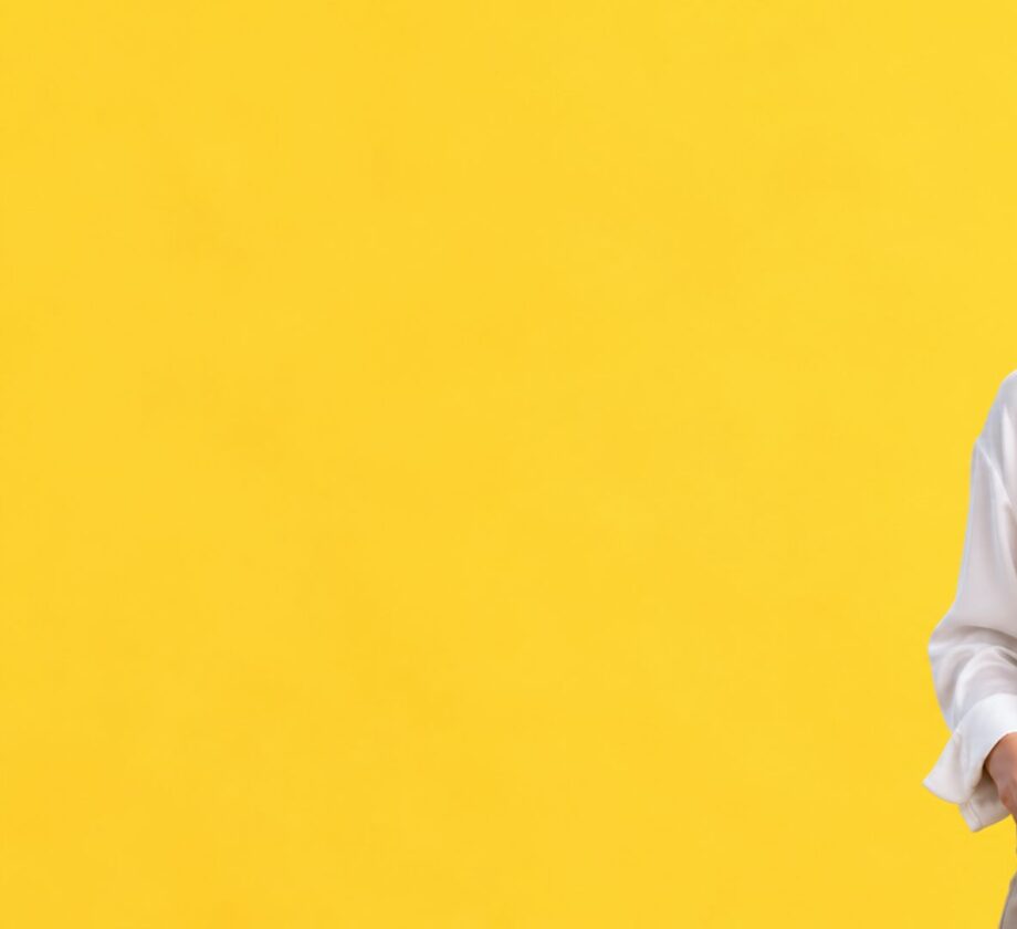 Mujer sonriente con camisa blanca hablando a su smartphone, ilustrando las búsquedas por voz y las nuevas formas de interacción con inteligencia artificial.