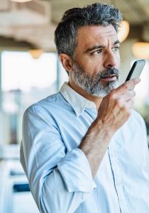 Directivo hablando por voz con su móvil en una oficina moderna y luminosa.