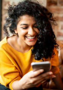 Mujer sonriendo mientras utiliza su smartphone, una imagen del uso cotidiano del móvil para consultar información y descubrir productos y servicios.