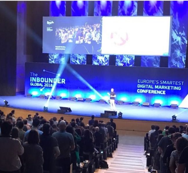 Escenario principal de The Inbounder Global 2018, con ponente en directo y público asistente en un auditorio lleno, durante la conferencia europea sobre marketing digital organizada con el apoyo de MacLucan y WAM Global.